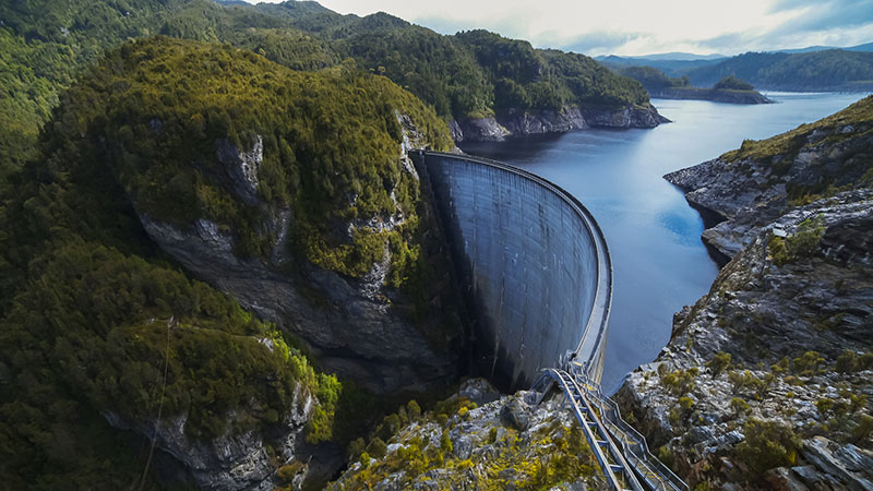 An aerial photo of the Gordon Dam in South West Tasmania, highlighting the stark contrast of the hydroelectric structure and the beauty of surrounding wilderness. 